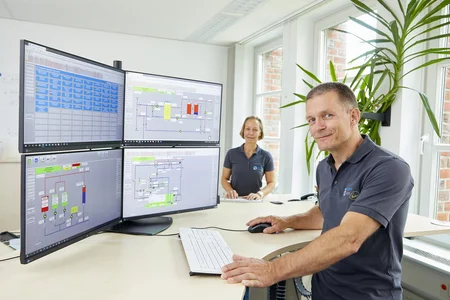 Zwei Fachkräfte von RegioEnergie , die vor mehreren Bildschirmen sitzen auf denen komplexe Energiesystem-Grafiken abgebildet sind. 
