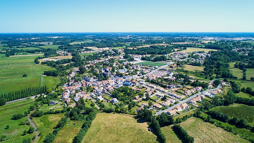 Luftaufnahme eines kleinen Dorfes, das in mitten grüner Felder liegt.
